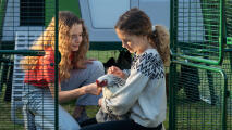 Two girls petting a chicken within the Eglu pro chicken coop run