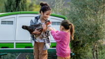 Two girls playing and cuddling a chicken next to the Eglu pro chicken coop