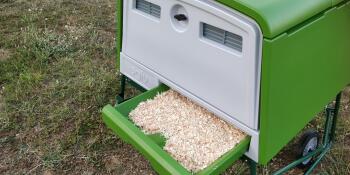 A litter tray with bedding pulled half way out of the green Cube chicken coop