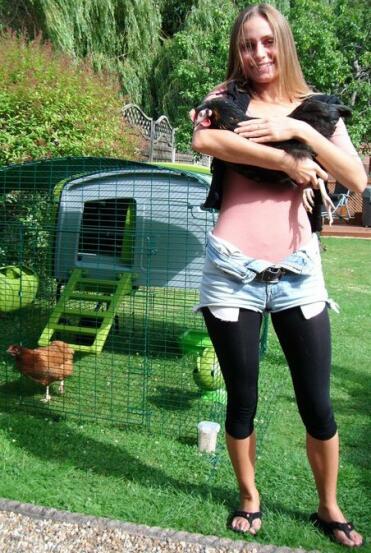 Lady holding chicken with green Omlet Eglu Cube large chicken coop and run behind her