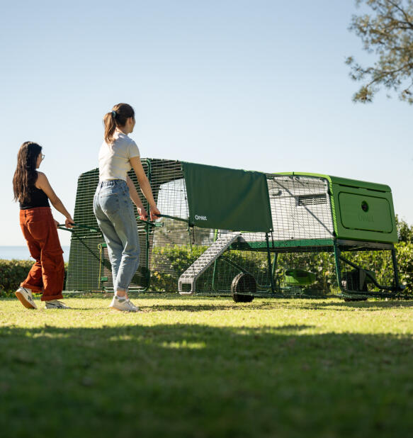 Two women pulling the Eglu pro chicken coop across a lawn