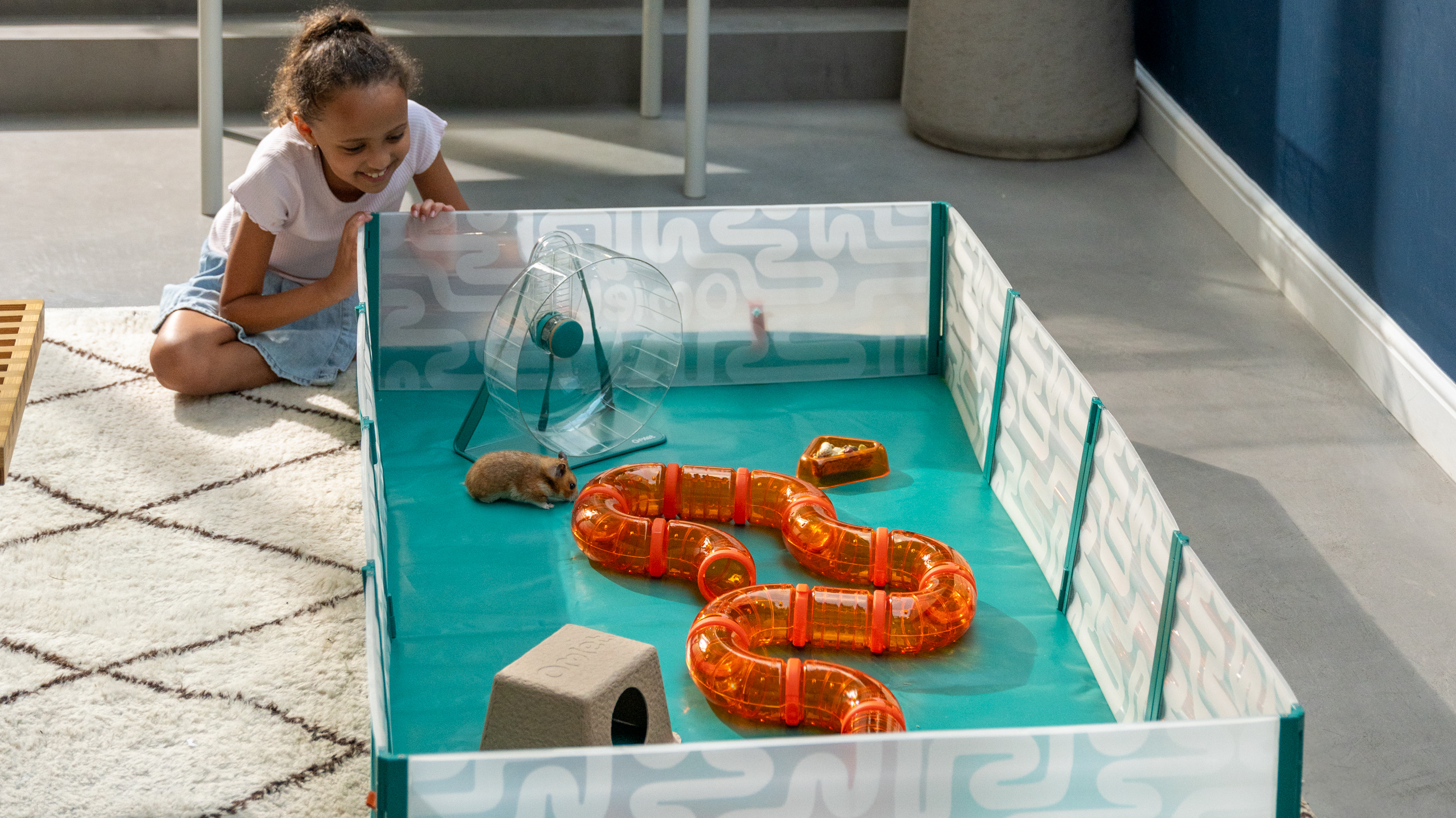 Girl sat next to Omlet Hamster Playpen with tunnels, a wheel and hideouts inside